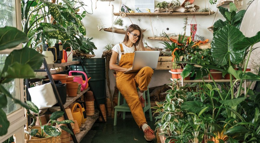 Eine Frau sitzt mit einem Laptop in einer Gärtnerei